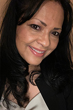 The image shows a woman smiling at the camera with her hair styled upwards and wearing a dark top.