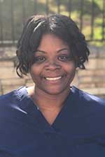 The image shows a woman wearing a blue scrub top, smiling at the camera, with her hair styled in an afro.