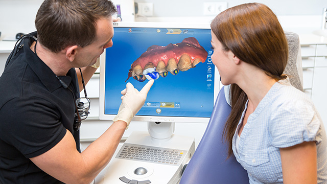 A dental professional showing a 3D model of a tooth to a patient during a consultation.