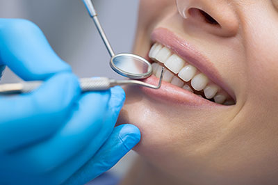 An individual receiving dental care with a smile on their face, while a dental professional works on their teeth using instruments visible through a magnifying glass.