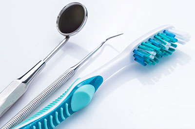 The image shows a collection of dental tools including a toothbrush with blue bristles, a pair of silver scissors, and a metal loop instrument, all placed on a white surface.