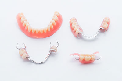 The image shows a collection of dental appliances displayed on a white background, including braces, retainers, and a partial denture with pink acrylic teeth, arranged in two rows for comparison purposes.