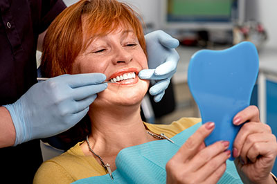 A woman sitting in a dental chair with a blue mouthguard, receiving dental care from a professional who is adjusting her bite guard while wearing gloves and a mask.