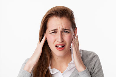 The image shows a woman with her hand on her head, appearing to be experiencing discomfort or pain, possibly related to a medical condition or stress.