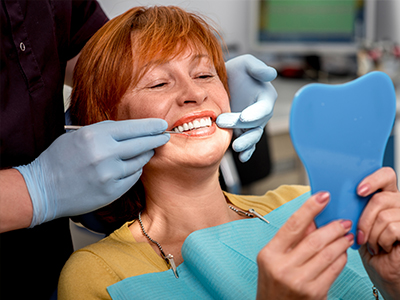 A woman receiving dental care with a smile on her face, while holding up a blue mouthguard for inspection.