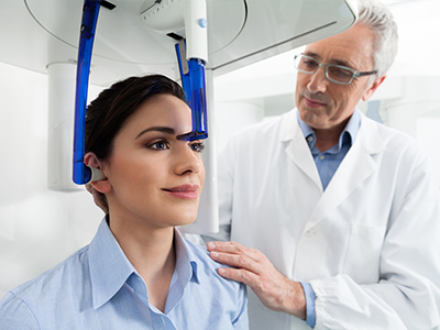 A medical professional in a white coat is assisting a woman with a blue device on her head, likely for a medical procedure or examination.