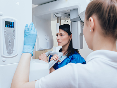 A woman wearing blue gloves is standing in front of a large 3D scanner machine, while another person observes the process.