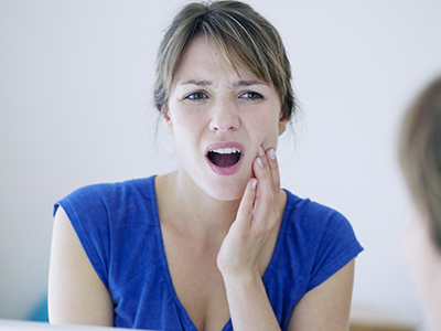 Woman with hand on face, making an expression of surprise or distress, while sitting in front of mirror.