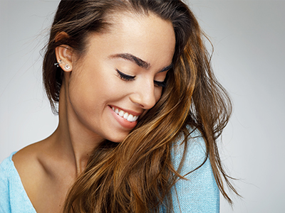 A woman with long hair and a serene expression, smiling slightly while looking downwards, against a plain background.