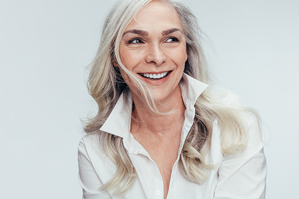 The image shows a woman with short blonde hair smiling at the camera while wearing a white top.