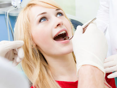 A woman receiving dental care with her mouth open, wearing a red shirt, while a dental professional works on her teeth.