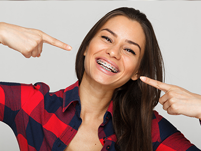 A woman with a wide smile pointing towards her teeth, holding up her index finger for emphasis.